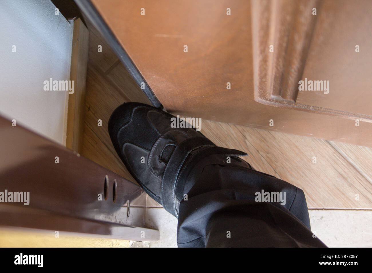 Image de la chaussure et du pied d'un homme au milieu de la porte. Référence aux vendeurs et aux fraudeurs les plus agressifs. Banque D'Images