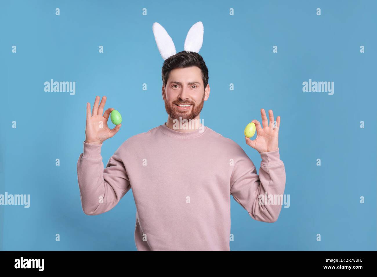 Un homme heureux dans un joli bandeau d'oreilles de lapin tenant des œufs de Pâques sur fond bleu clair Banque D'Images