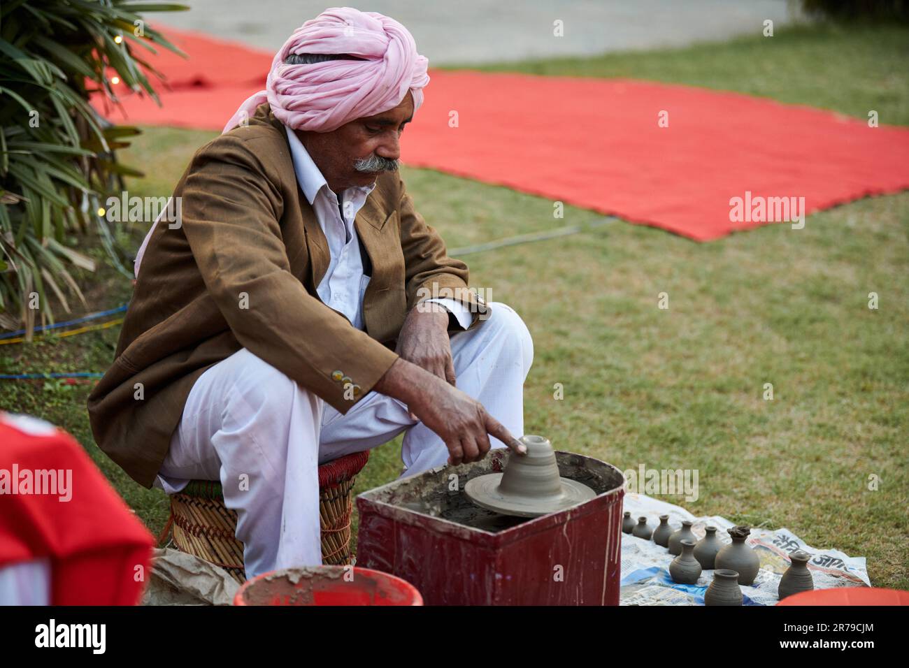 New Delhi, Inde - 10.12.2022 - l'ancien sikh indien en robe de tête de pagri rose, pantalon blanc et blouson marron fait des articles de poterie d'argile, vieux cré de potier Banque D'Images