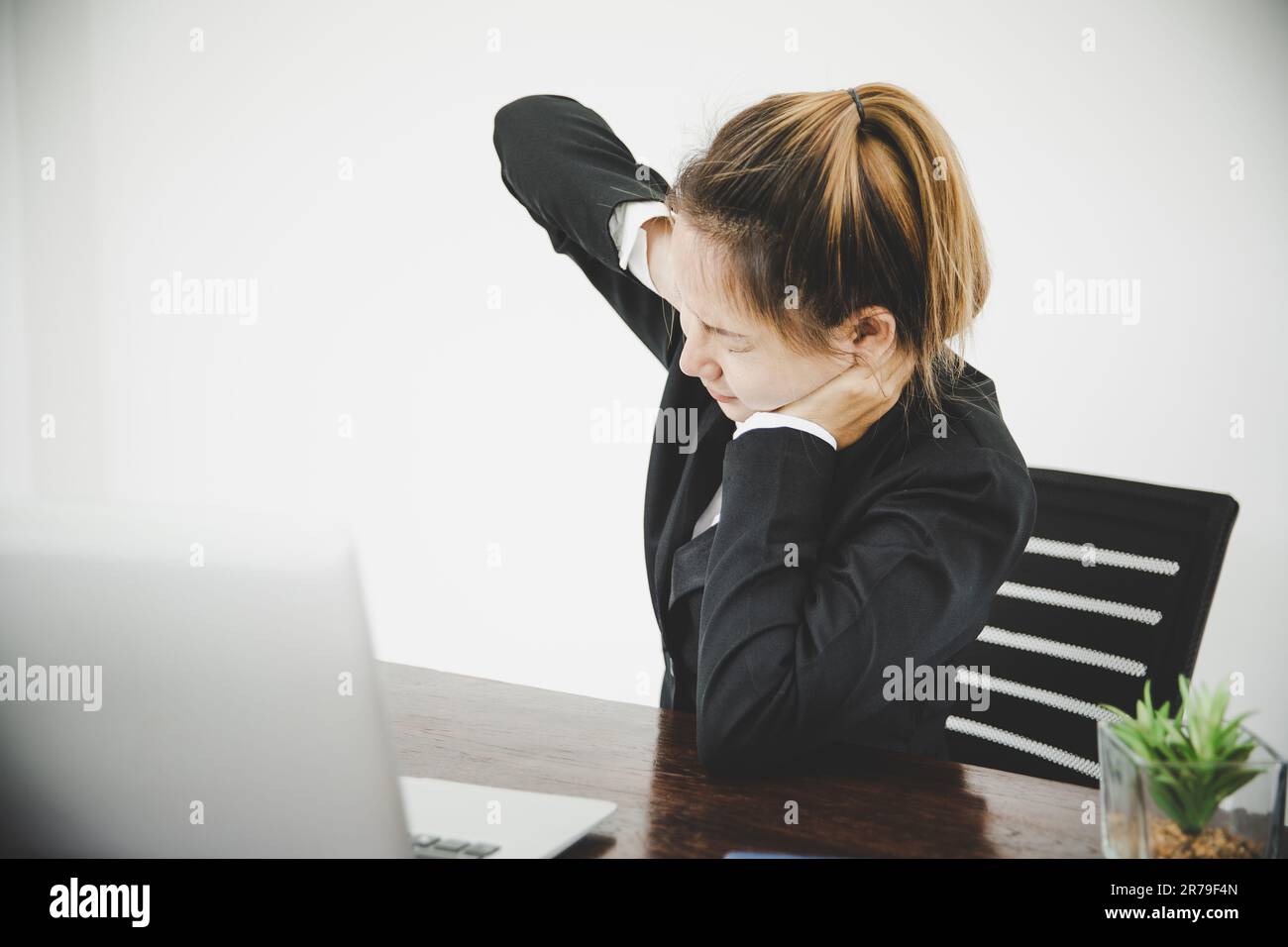 La jeune femme asiatique est assise au travail et a de la douleur dans le cou pendant qu'elle est assise dans le bureau de travail Banque D'Images