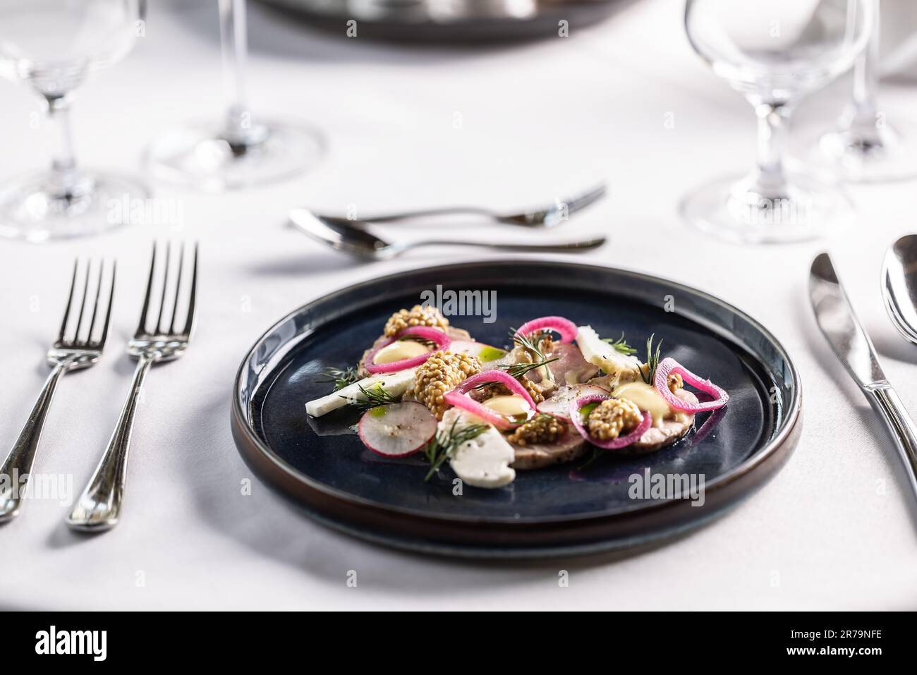 Une touche moderne sur le pâté de foie de canard présenté avec des légumes sur une assiette sombre sur une table de restaurant. Banque D'Images