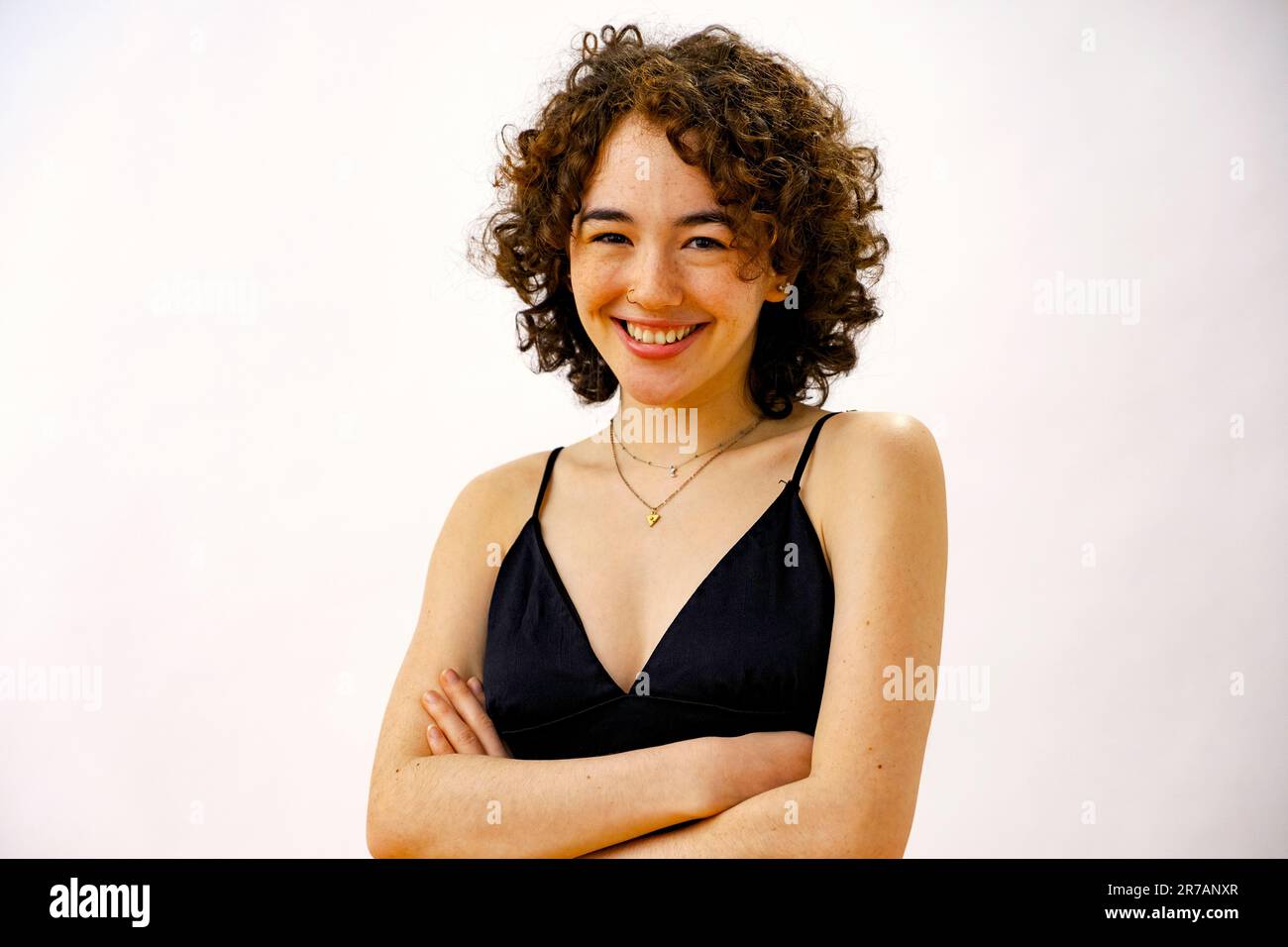 jeune femme aux cheveux bouclés et aux bras croisés souriant en regardant l'appareil photo Banque D'Images