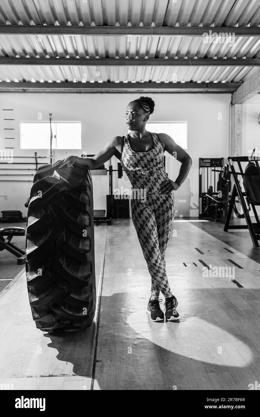 Une femme noire sportive et ajustée qui se pose en toute confiance près d'un pneu de gym Banque D'Images