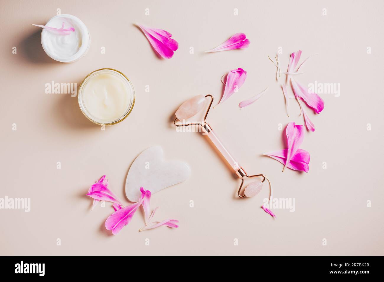 Rouleau de quartz rose, gua sha et crèmes pour le visage sur fond rose, soins du visage et du cou, soins spa. Banque D'Images