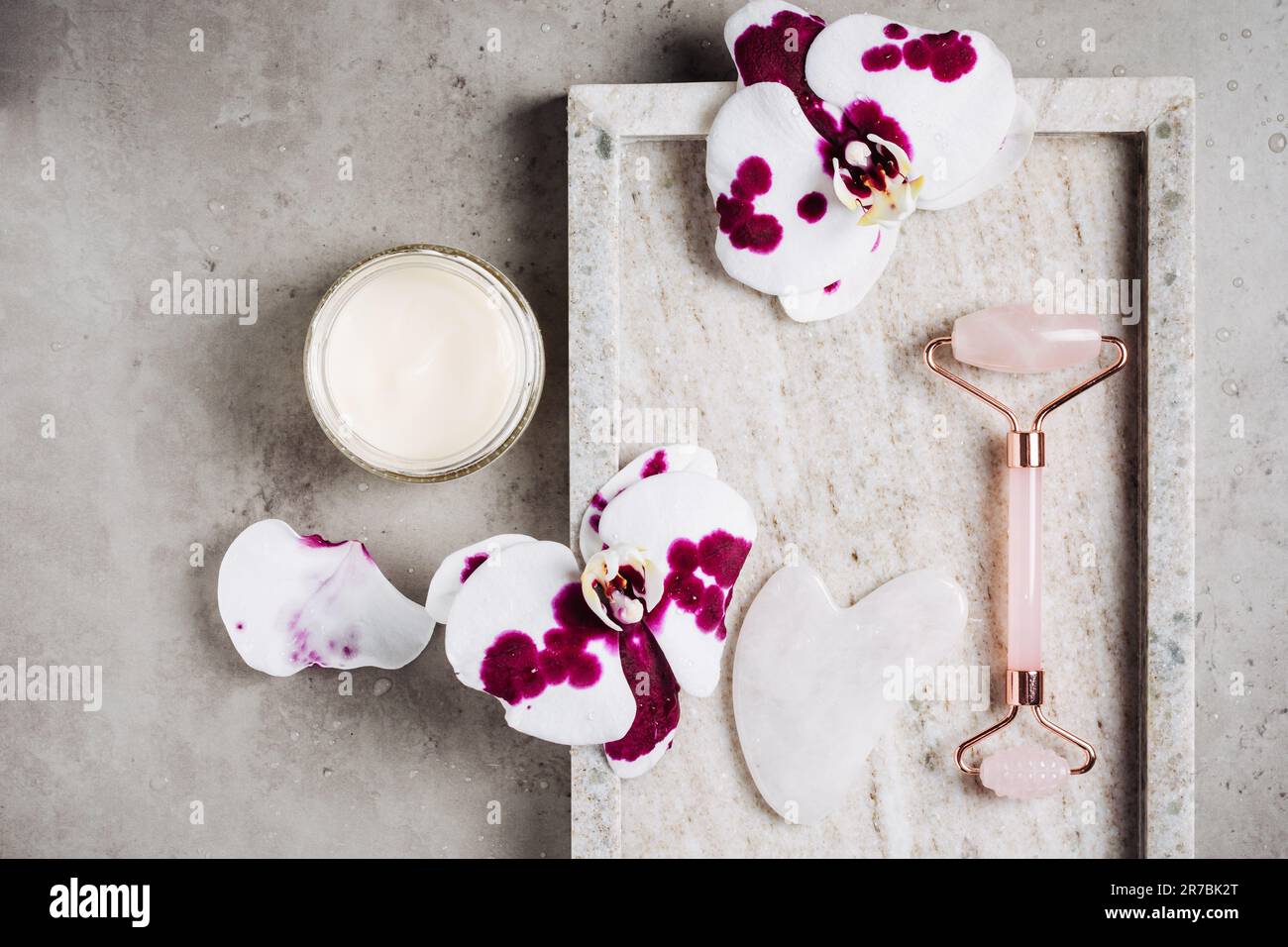 Rouleau à cadran en quartz rose, fleurs de SHA gua et d'orchidées sur fond de marbre. Concept spa, soin du visage. Banque D'Images