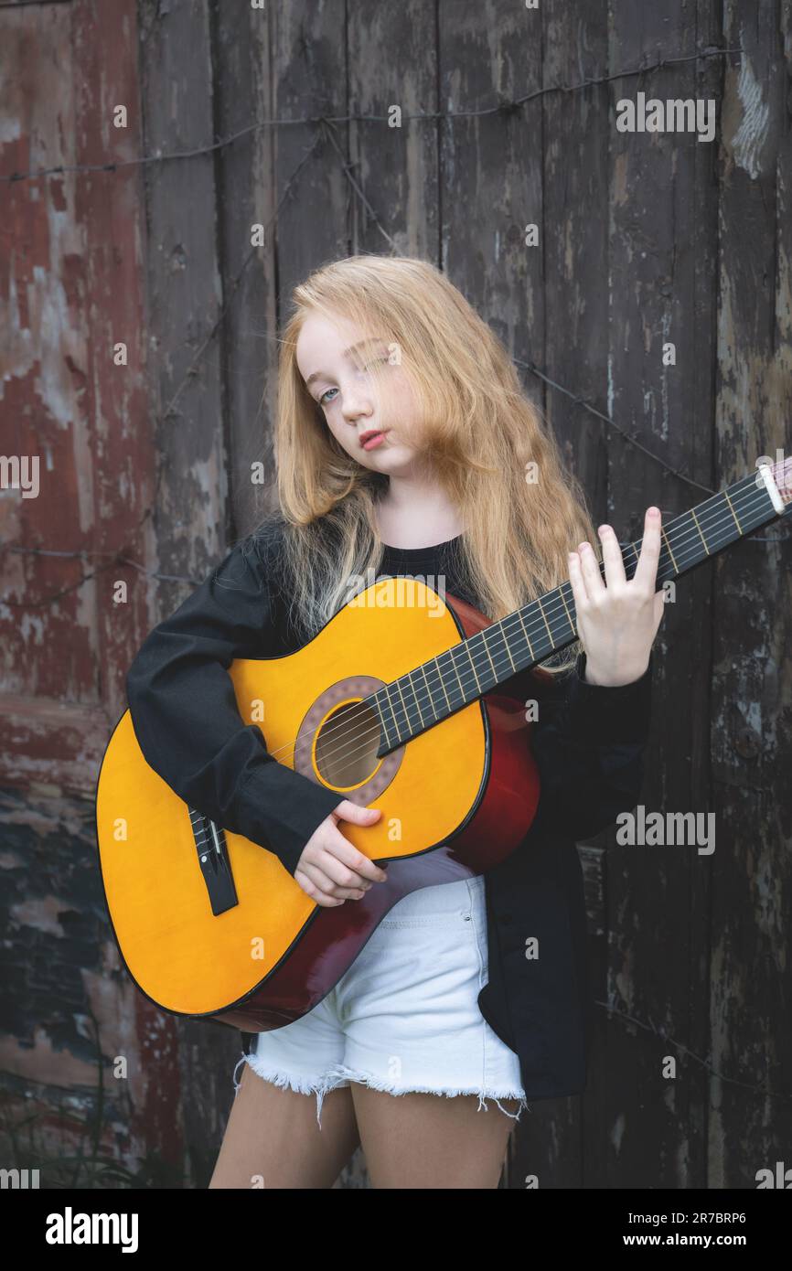 Une jeune fille avec une guitare dans la rue. Un jeune guitariste avec de longs cheveux blancs joue de la guitare. Banque D'Images