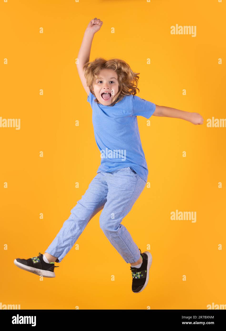 Toute la longueur de saut d'enfant excité. Enfant garçon de 8-9 ans dans un t-shirt saut isolé sur fond jaune. Concept de style de vie d'enfance. Maquette spa Banque D'Images