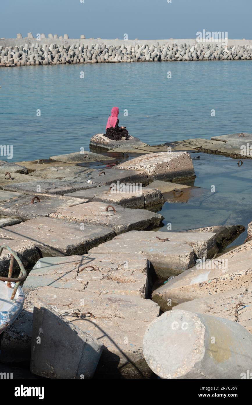 Alexandrie, Égypte. 1 décembre 2022 femmes musulmanes portant un hijab rose assis sur de grandes dalles de béton conçues pour protéger la côte méditerranéenne c Banque D'Images