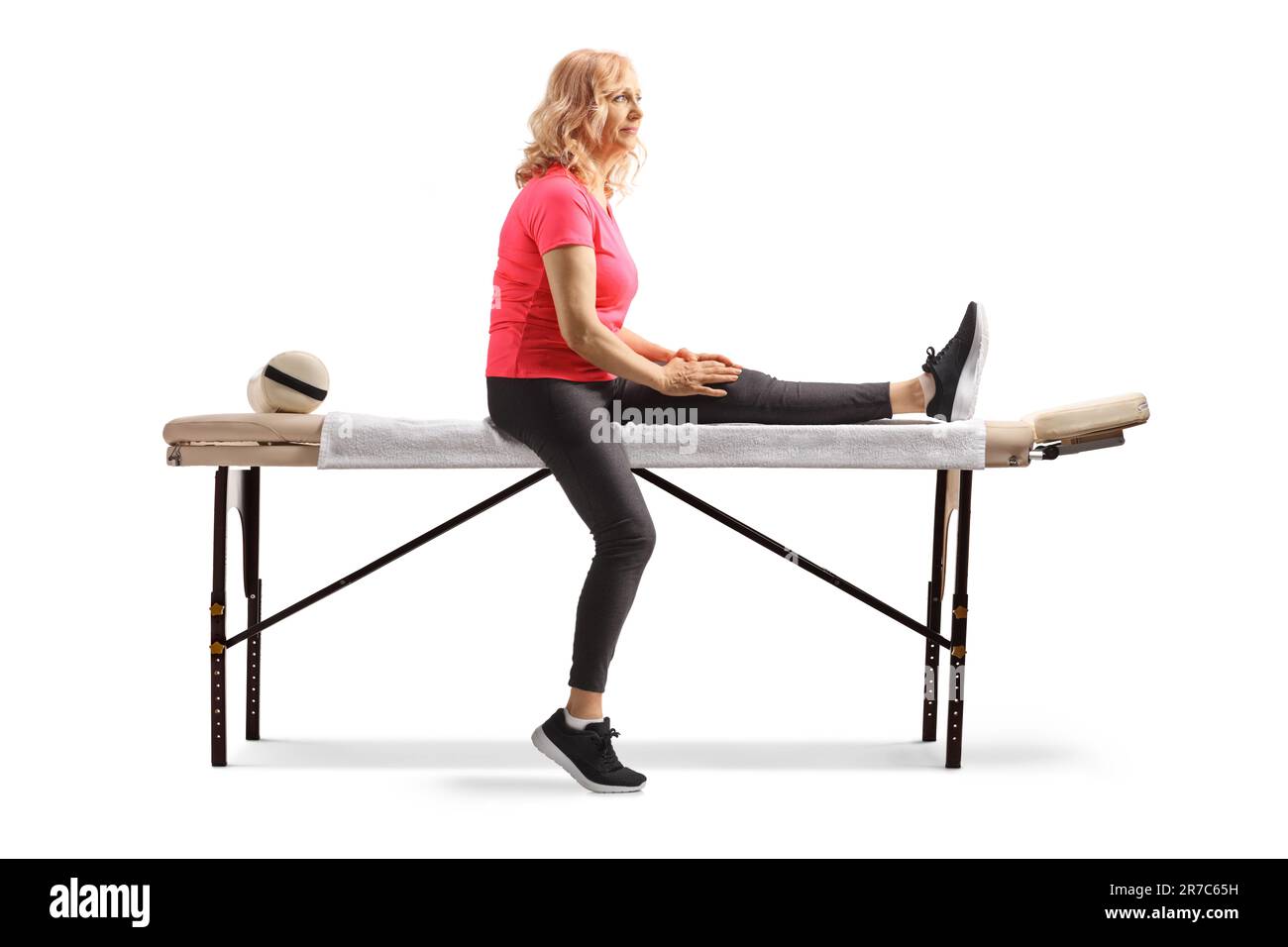 Femme mature avec une jambe blessée assise sur une table de thérapie isolée sur fond blanc Banque D'Images