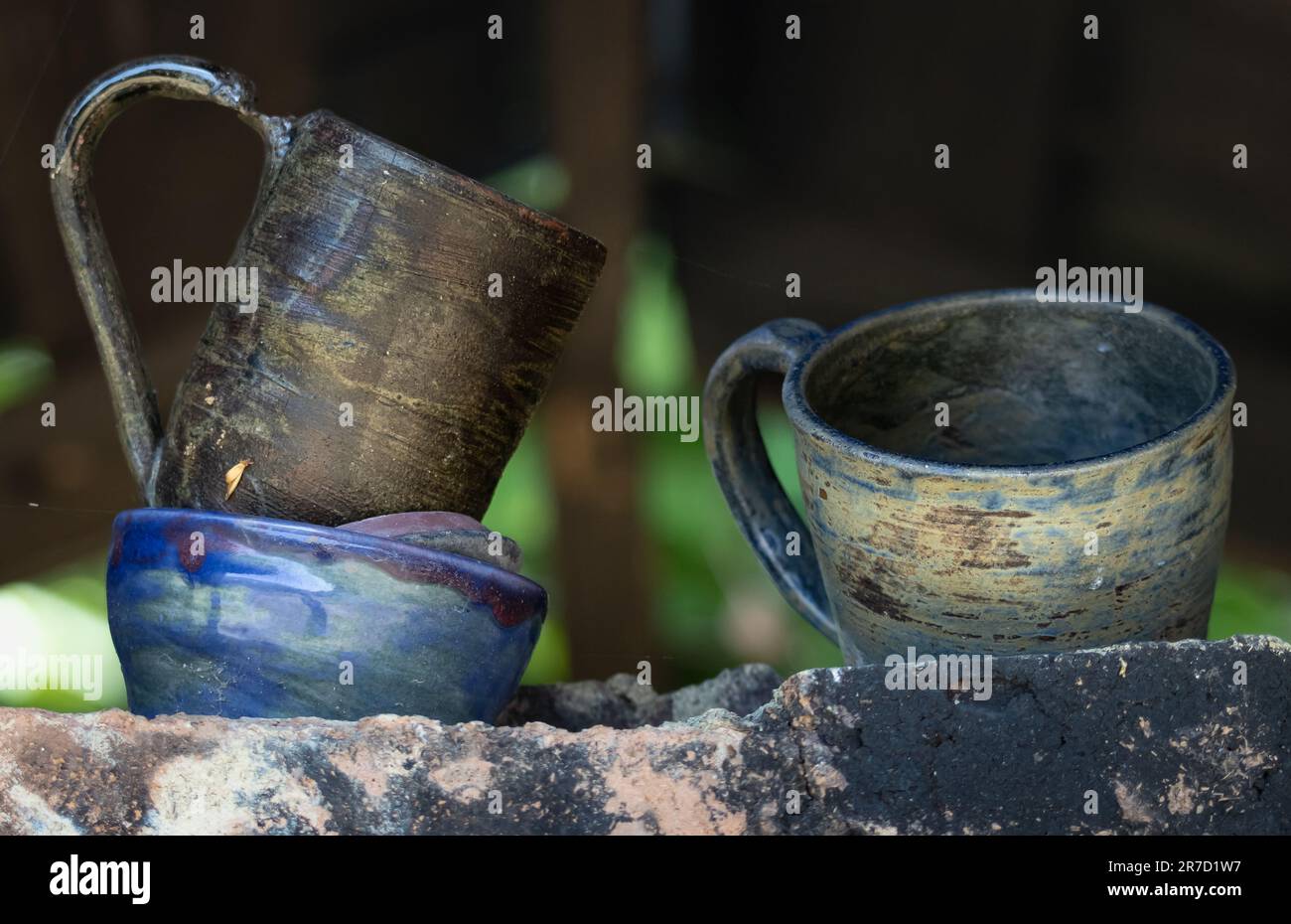 Trois objets de poterie imparfaits faits à la main, deux tasses aux tons naturels et un bol aux tons bleus, prêts à être jetés assis sur une étagère en pierre à l'extérieur Banque D'Images