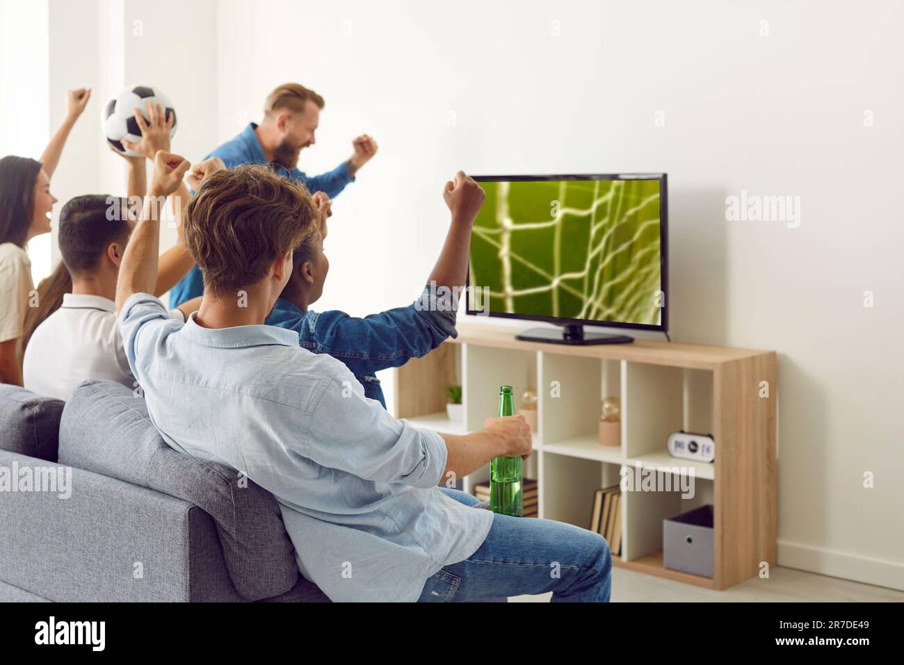 Groupe de jeunes amis heureux et enthousiastes regardant un match de football à la télévision à la maison Banque D'Images