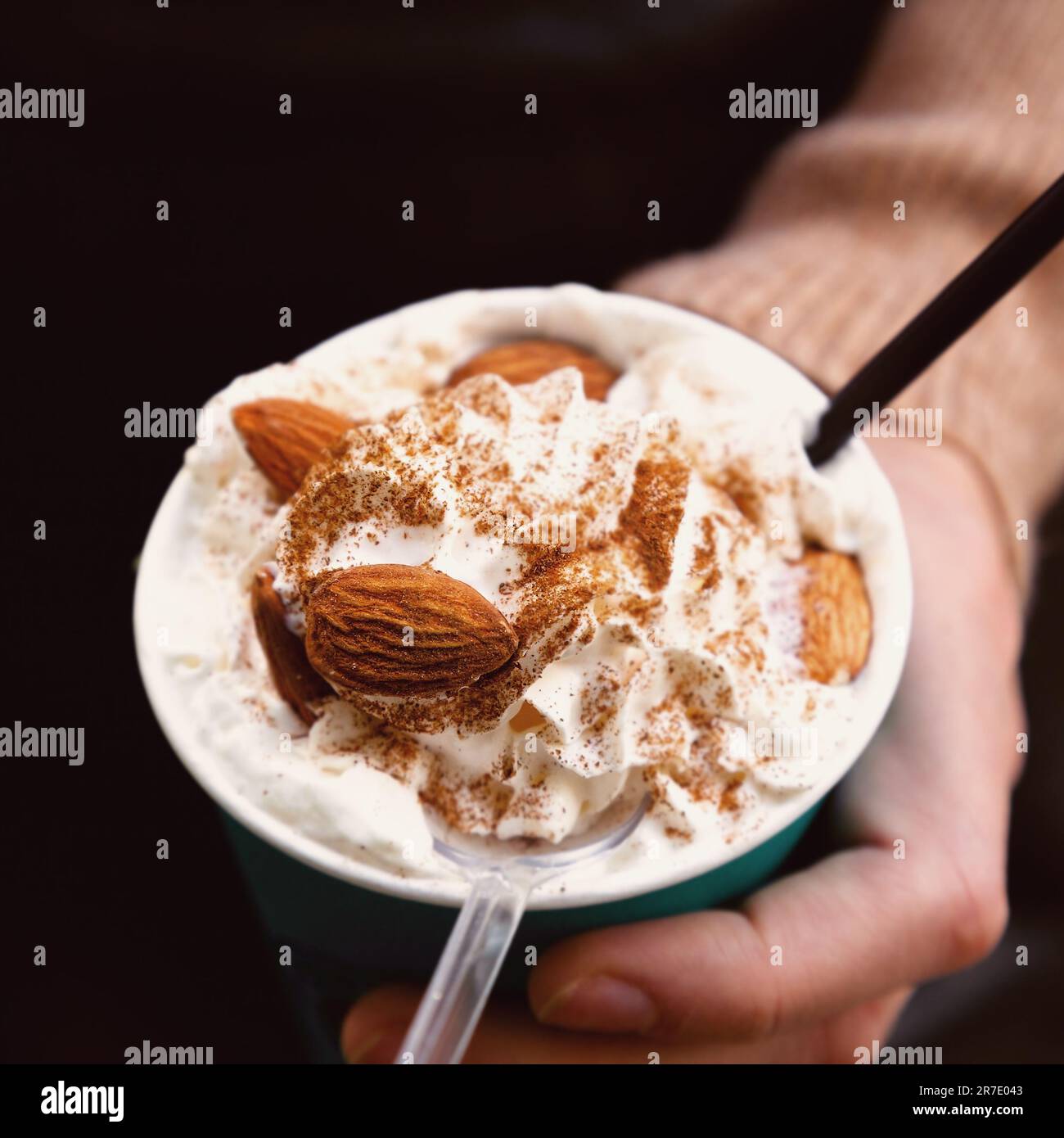 Fond défoqué main femelle tenant un verre de café avec de la crème. Concentrez-vous sur les amandes. Banque D'Images