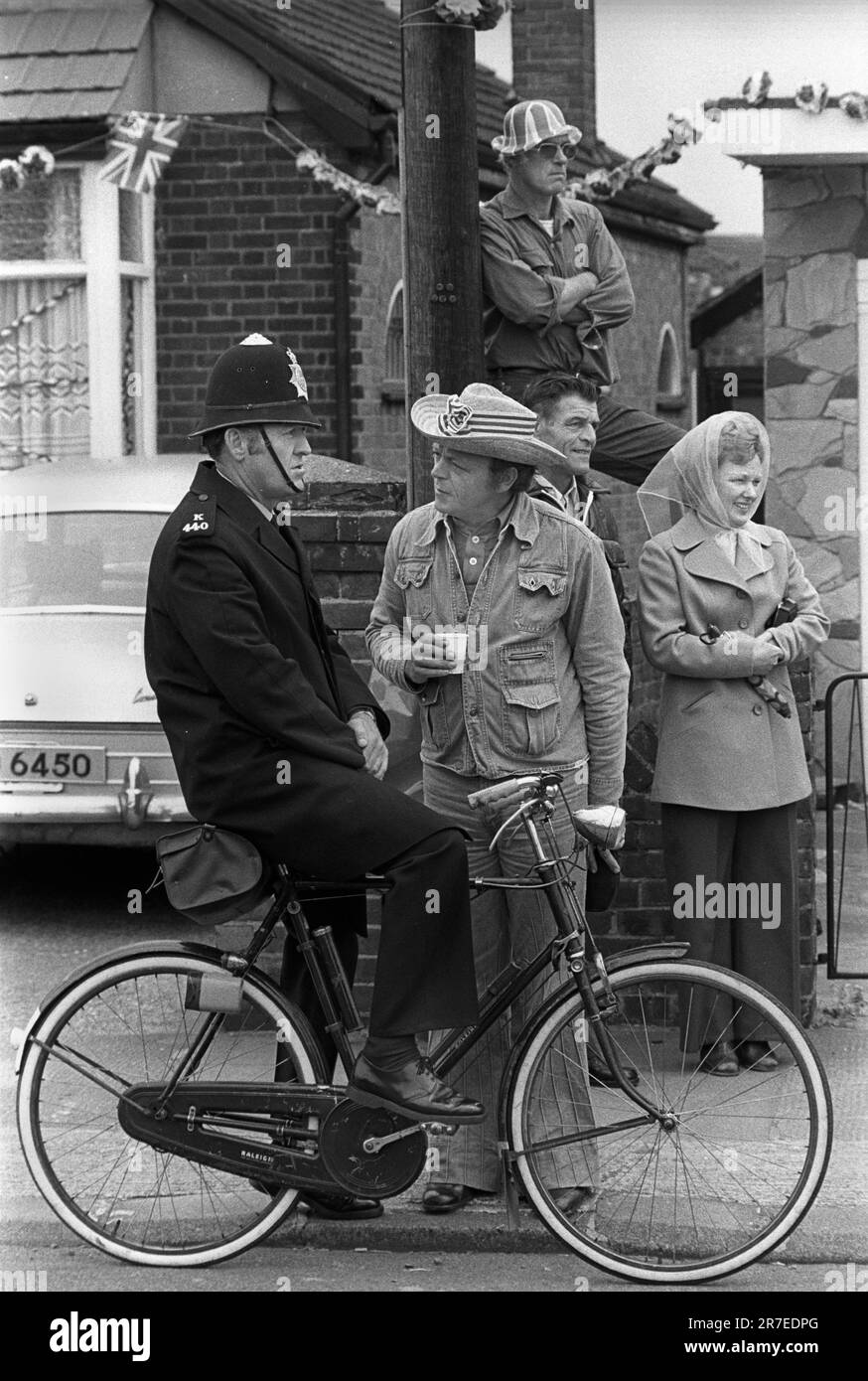 Reine Elizabeth II célébration du Jubilé d'argent 1977. Spring Bank Holiday Monday les résidents Betterton Road tiennent une fête célébrant la rue du Jubilé d'argent.Une petite foule se réunit pour regarder la parade avec un policier local sur son vélo. Rainham, Essex, Angleterre 6th juin 1977. Banque D'Images