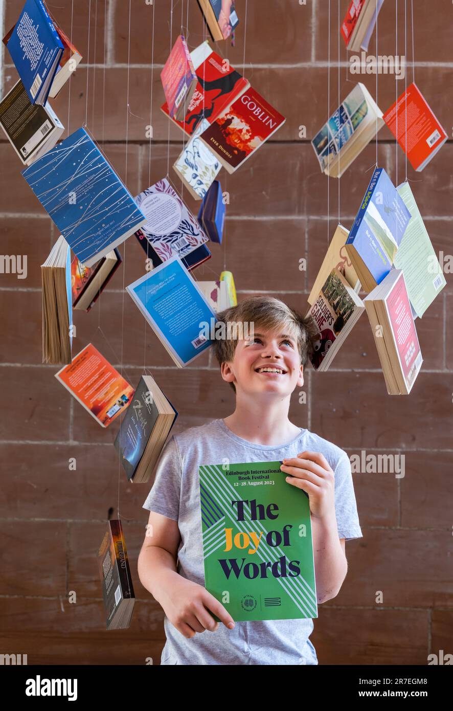 Un garçon de 12 ans lit le programme du Edinburgh International Book Festival 2023 entouré de livres de poche pour le lancement du programme, Écosse, Royaume-Uni Banque D'Images