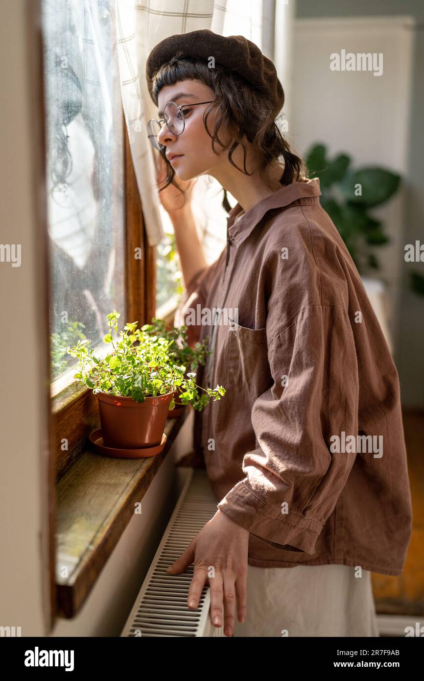 Une fille hipster solitaire triste qui regarde la fenêtre tout en passant du temps à la maison Banque D'Images