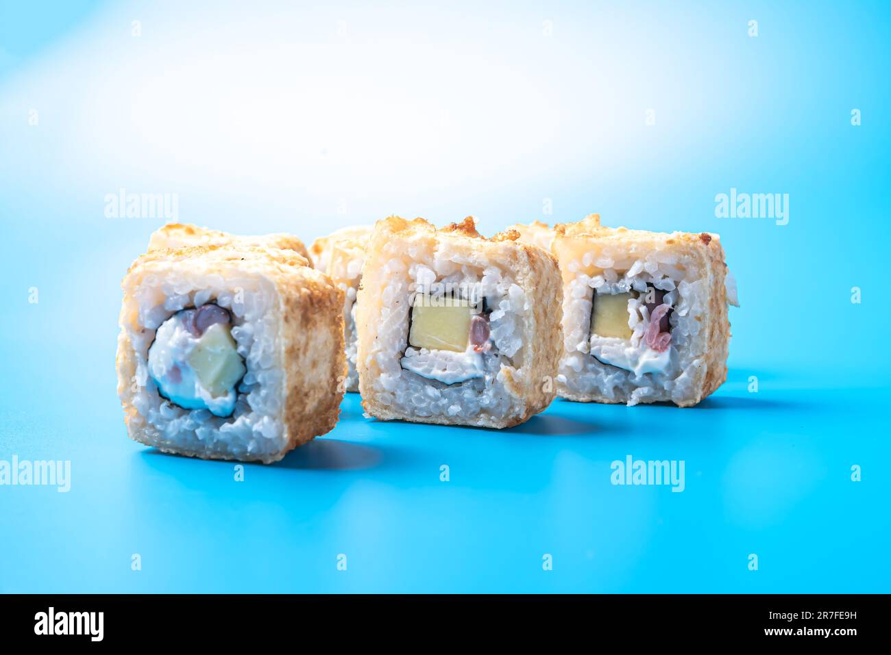 Petits pains à sushis aux crevettes, concombres et fromages, cuits dans une omelette, sur fond bleu. Photo de haute qualité Banque D'Images