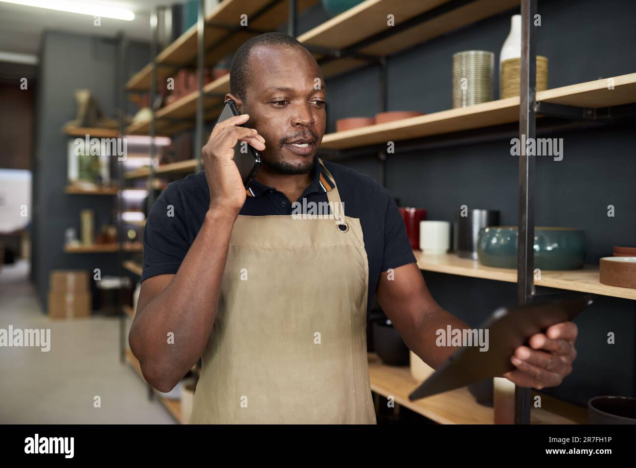 Directeur de studio de poterie africain utilisant un téléphone et une tablette dans un atelier Banque D'Images