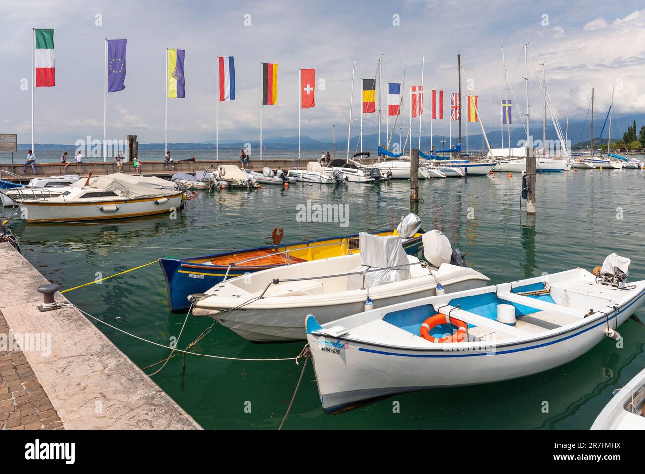 Petits bateaux et yachts amarrés dans le port de Bardolino avec des drapeaux européens au mur du port. Bardolino, Lac de Garde, Italie, Europe Banque D'Images