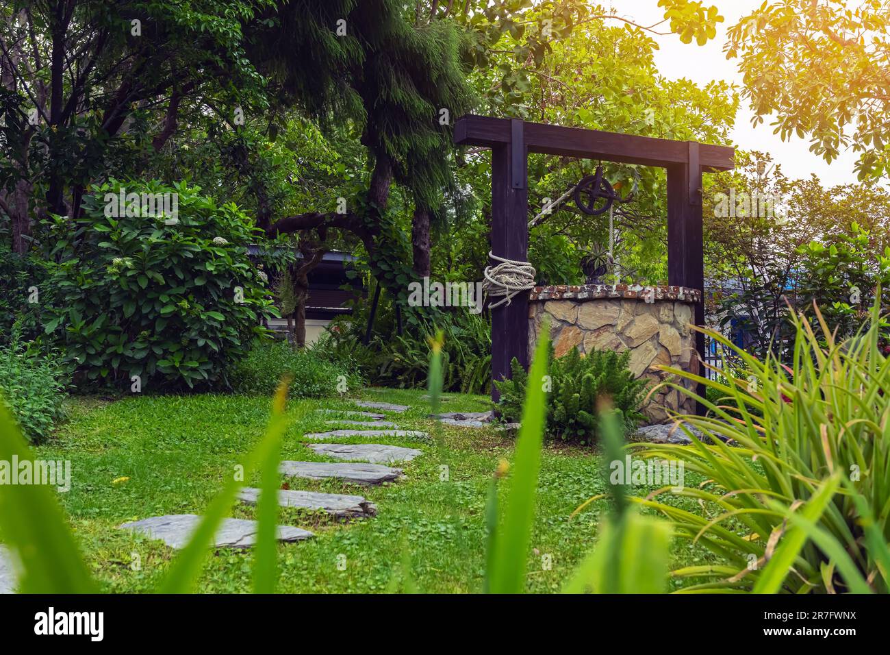 Magnifique bien artesian fait de pierres et poulie de roue avec seau en métal et corde dans une atmosphère paisible de jardin. Puits rétro en pierre dans la zone rurale Banque D'Images