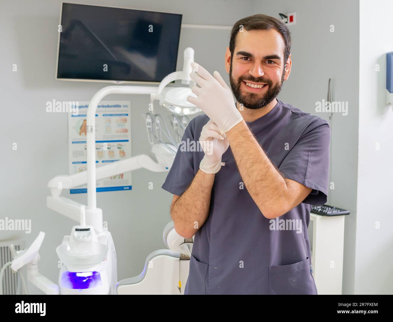 Un jeune dentiste met ses gants dans une clinique dentaire pendant un examen clinique Banque D'Images