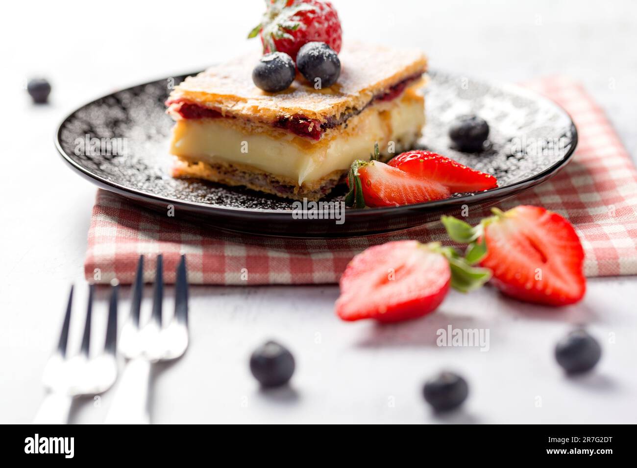 Un morceau de gâteau Napoléon aux graines de pavot et aux cerises, décoré de fraises et de bleuets sur un fond clair. Gros plan Banque D'Images