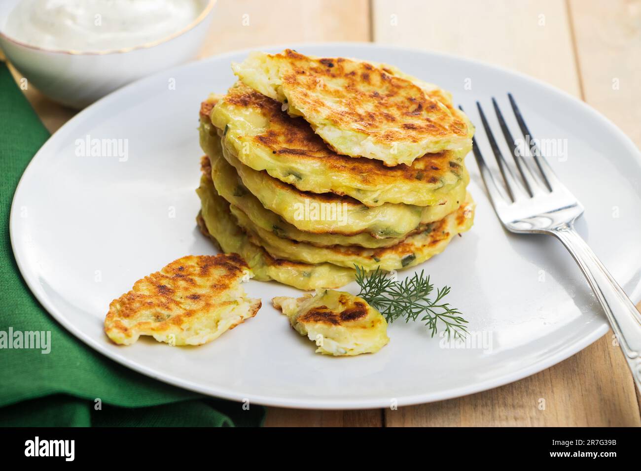 Une pile de beignets de courgettes dans une assiette et une sauce à la crème. Plat sur serviette verte. Alimentation végétalienne saine sur fond de bois. Banque D'Images