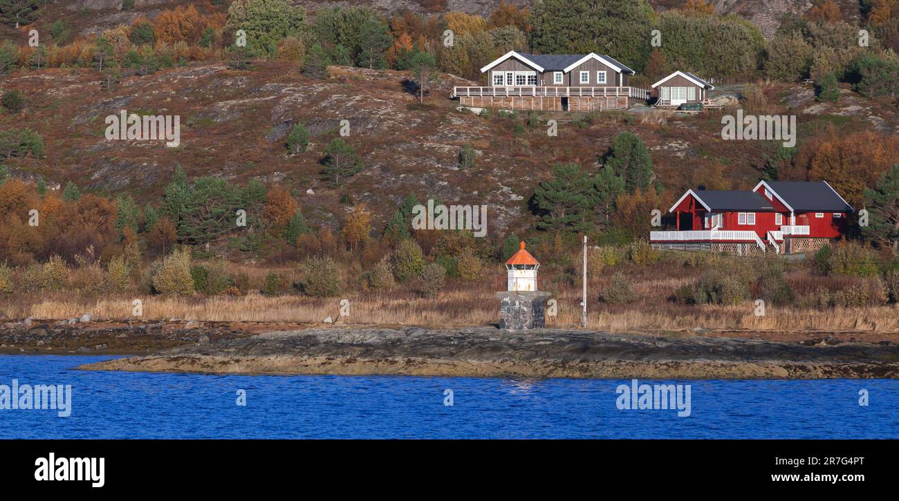 La tour blanche du phare avec son sommet rouge et ses maisons de campagne en bois se trouvent sur une côte rocheuse de la mer. Paysage norvégien panoramique Banque D'Images