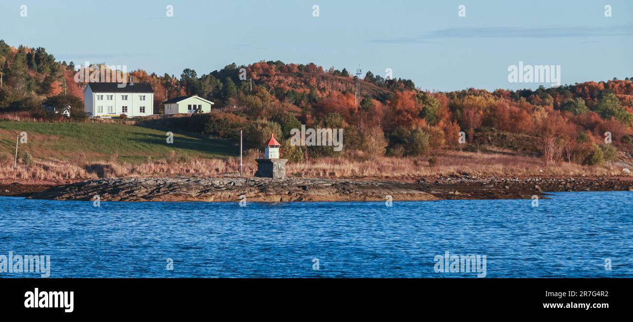 Paysage norvégien panoramique avec petite tour de phare et maisons de campagne en bois sur une côte rocheuse de la mer par une journée ensoleillée Banque D'Images