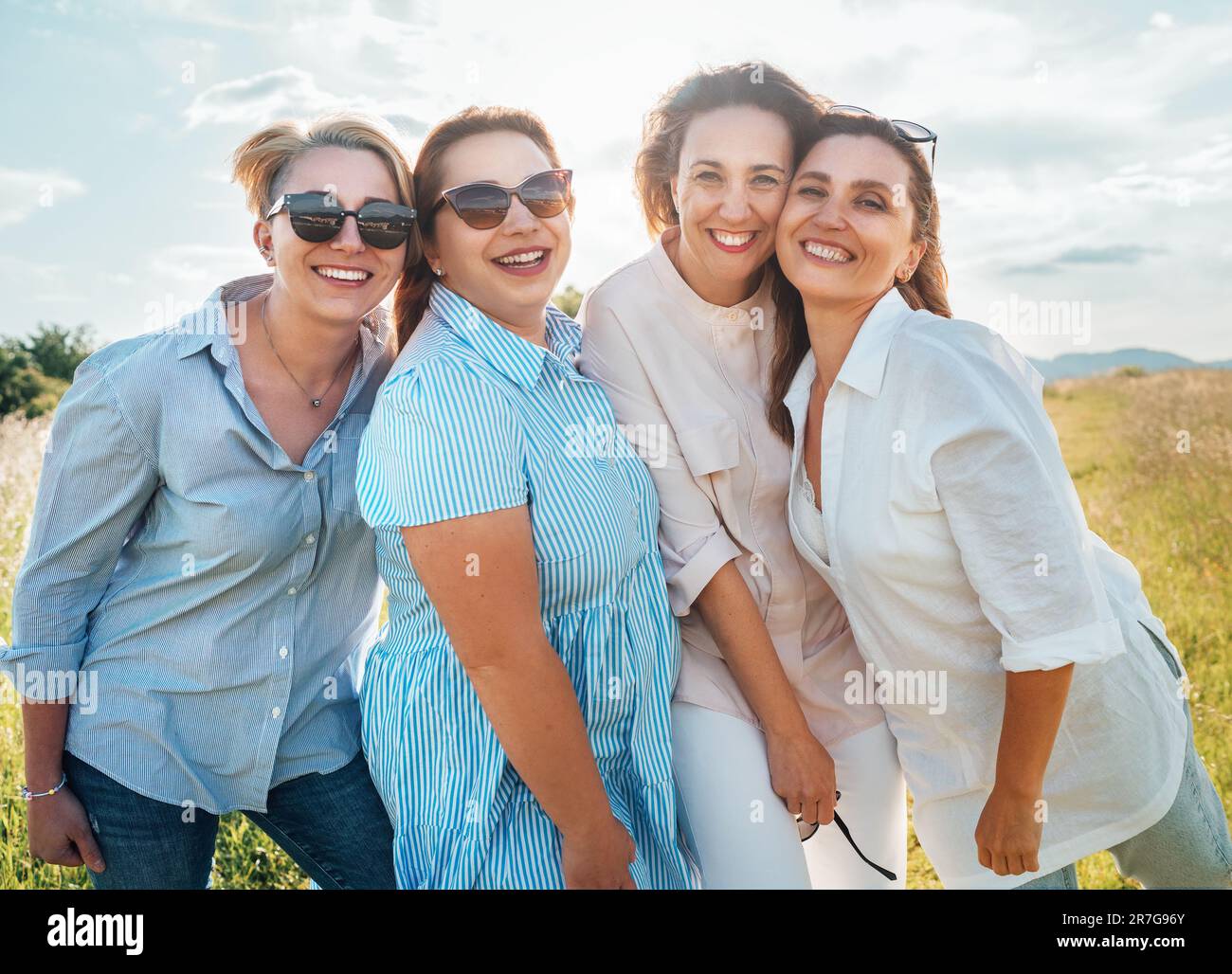Portraits de quatre femmes souriantes et gaies en lunettes de soleil embrassant et regardant l'appareil photo pendant la marche en plein air avec un rétroéclairage lumineux et ensoleillé. ven femme Banque D'Images