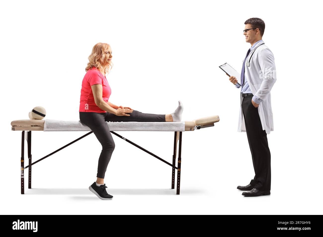 Femme avec une jambe blessée assise sur une table de thérapie et parlant à un médecin isolé sur fond blanc Banque D'Images