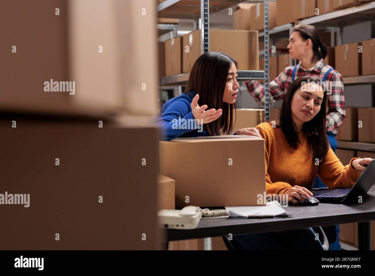 Les employés de l'entrepôt postal vérifient la conformité des livraisons et planifient la logistique sur ordinateur portable. De jeunes femmes asiatiques commandent des préparateurs discutant du ticket de cueillette des clients sur l'ordinateur dans le magasin Banque D'Images