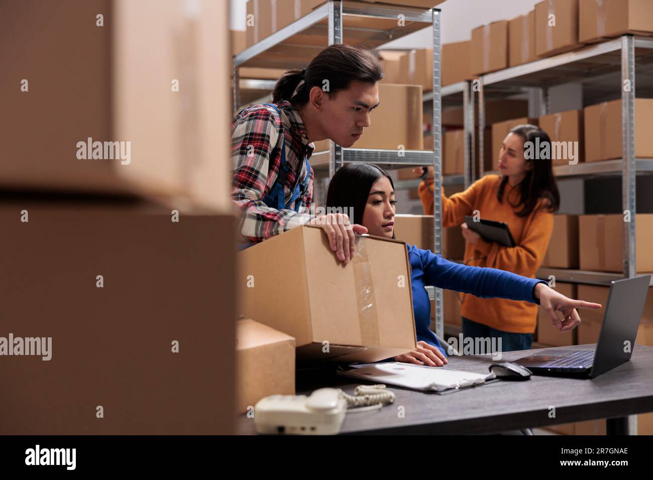 Le gestionnaire de colis de magasin et le gestionnaire d'expédition vérifient le bon de préparation de la commande sur l'ordinateur portable. Les employés d'entrepôt d'asie parlent du planning logistique et du plan sur ordinateur Banque D'Images