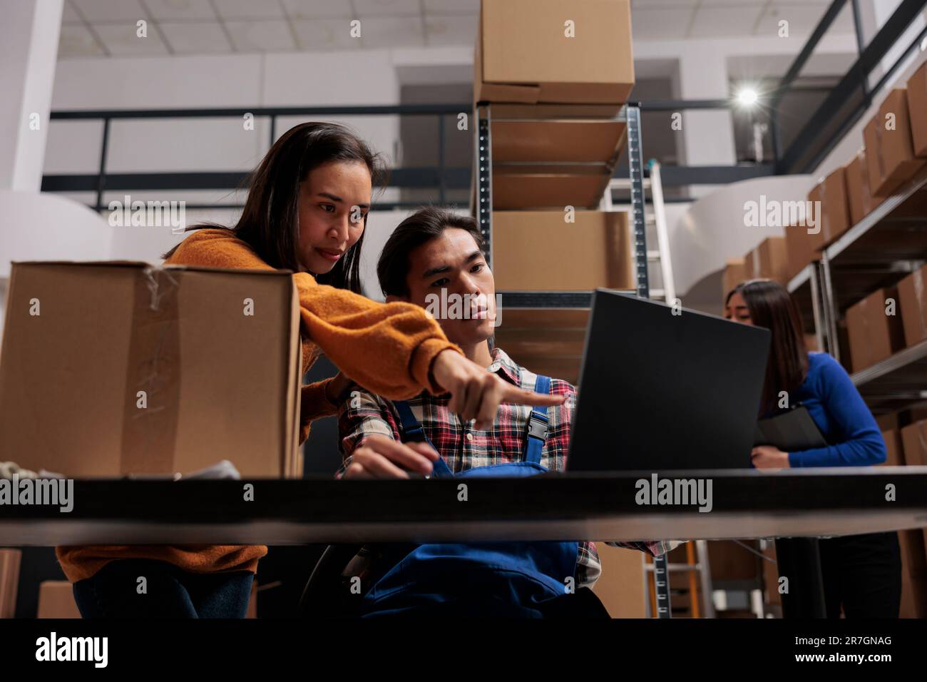 Le préparateur de commande et le responsable de la livraison du magasin analysent la liste de contrôle du client sur l'ordinateur portable dans la salle de stockage. Les travailleurs asiatiques des entrepôts qui pointent vers le calendrier de logistique des produits sur ordinateur Banque D'Images