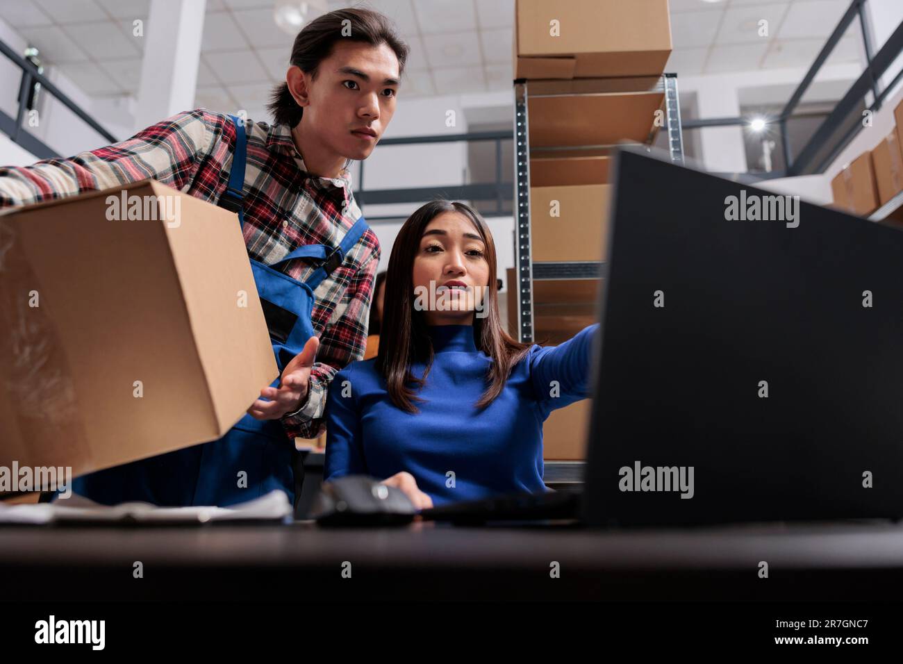 Les employés asiatiques de l'entrepôt de poste préparent le colis pour l'expédition. L'équipe des employés de la société d'expédition effectue la gestion des stocks à l'aide du logiciel sur l'ordinateur portable dans la salle de stockage Banque D'Images