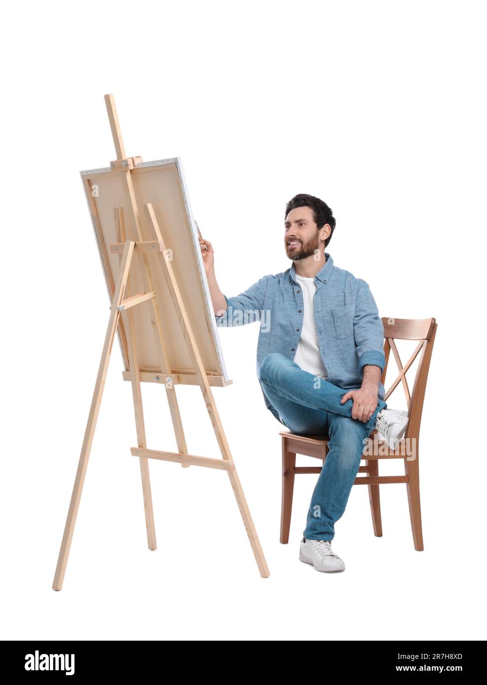 Joyeux homme peignant avec la brosse sur fond blanc. Utilisation du chevalet pour tenir la toile Banque D'Images