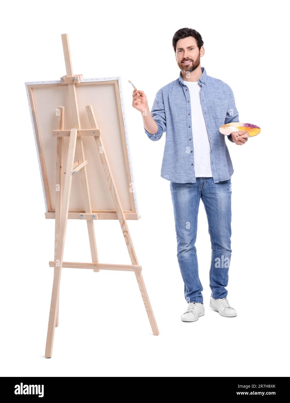 Joyeux homme peignant avec la brosse sur fond blanc. Utilisation du chevalet pour tenir la toile Banque D'Images