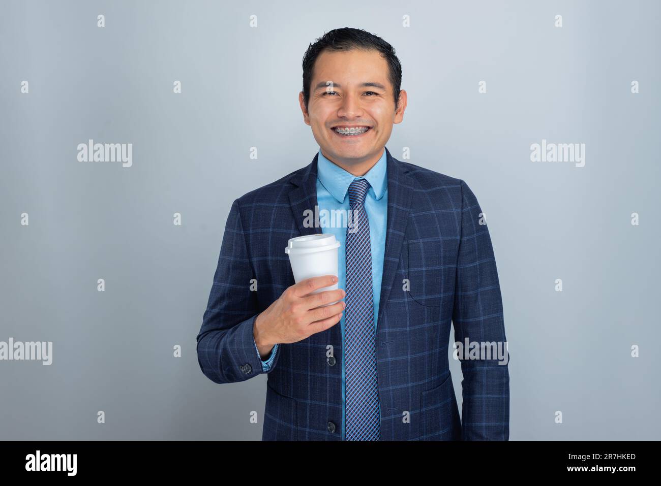 Jeune hispanique en costume bleu et sourit de cravate alors qu'il tient un café prêt pour le travail, une personne Banque D'Images