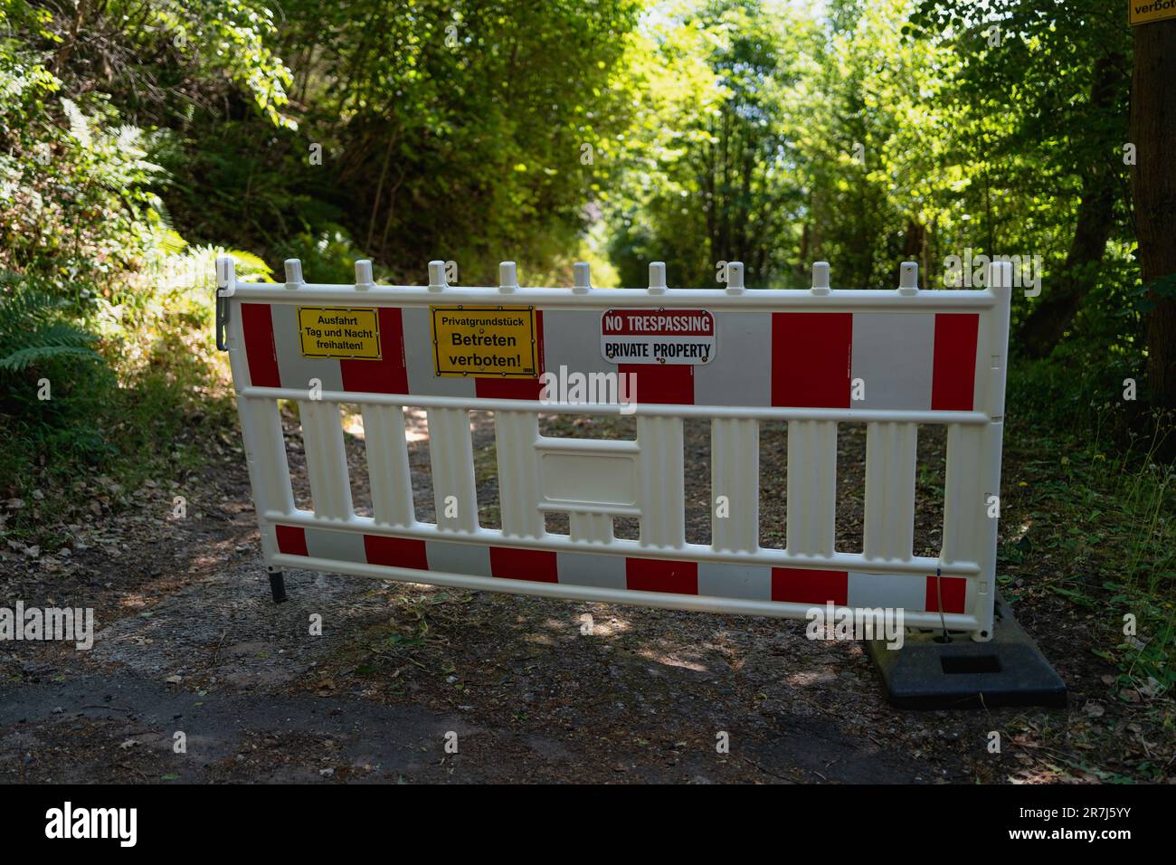 Barrière routière bilingue avec panneaux « sans intrusion » en allemand et en anglais, bloquant l'accès à la propriété privée dans la forêt Banque D'Images