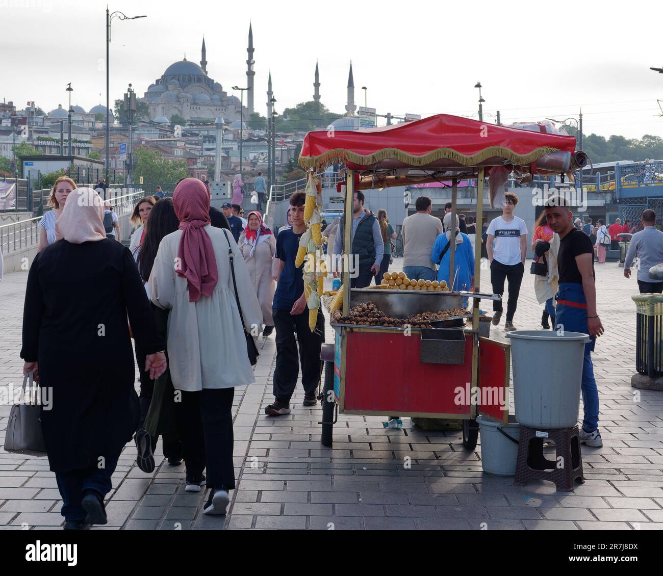 Des femmes musulmanes passent devant une charrette vendant du maïs sucré dans le district de Eminönü avec la mosquée Suleymaniye au loin, Istanbul, Turquie Banque D'Images