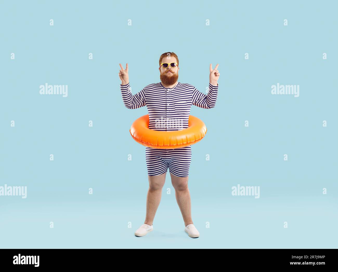 Drôle chubby homme avec cercle gonflable pour la natation à la taille montre V-signe sur fond bleu clair. Banque D'Images