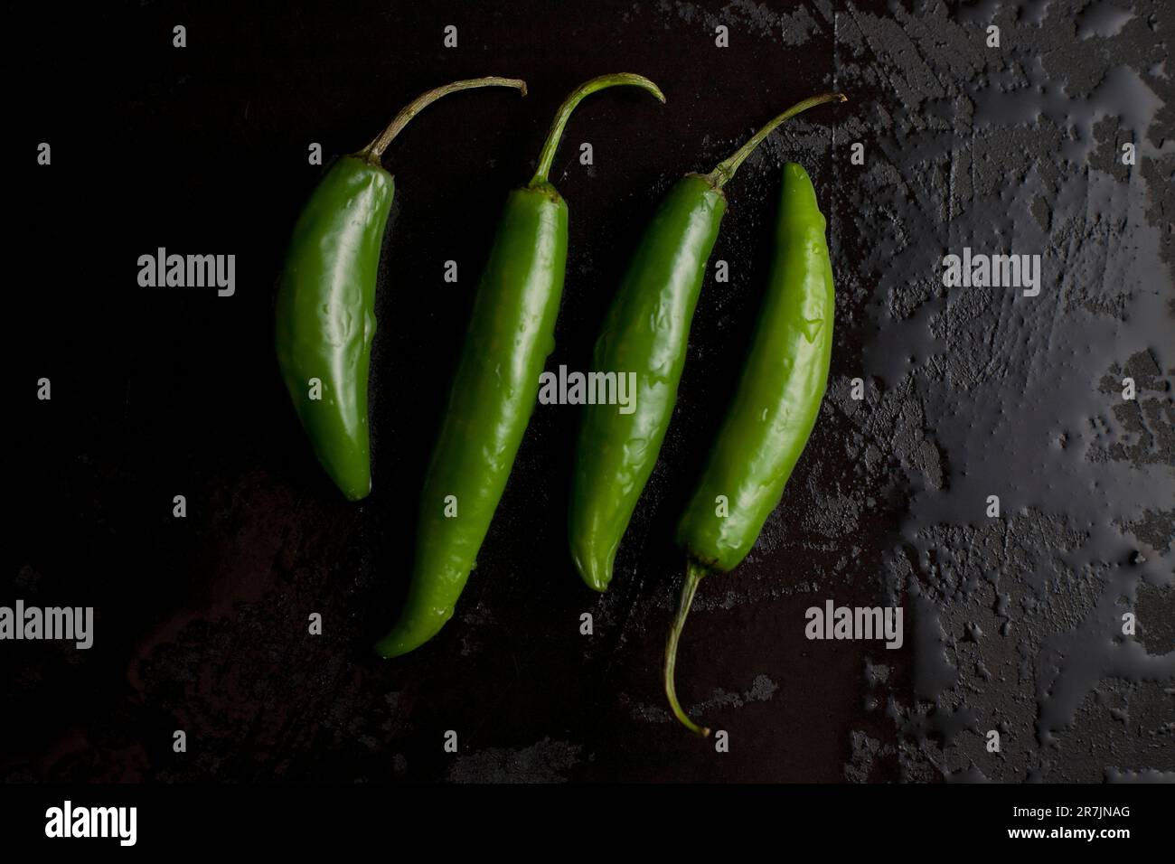 Quatre poivrons verts chauds biologiques sont assis sur une planche à découper noire humide dans une cuisine à Seattle, Washington. Banque D'Images