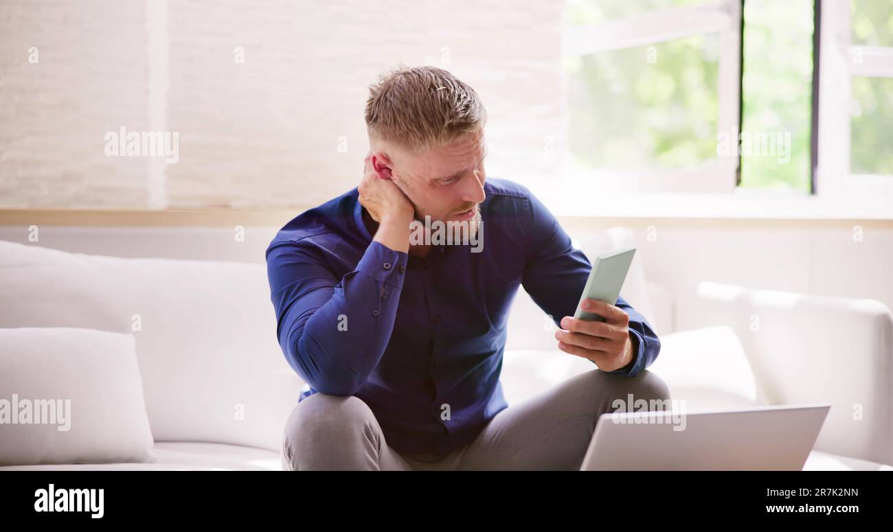 Homme avec douleur de cou assis à l'aide d'un téléphone mobile Banque D'Images