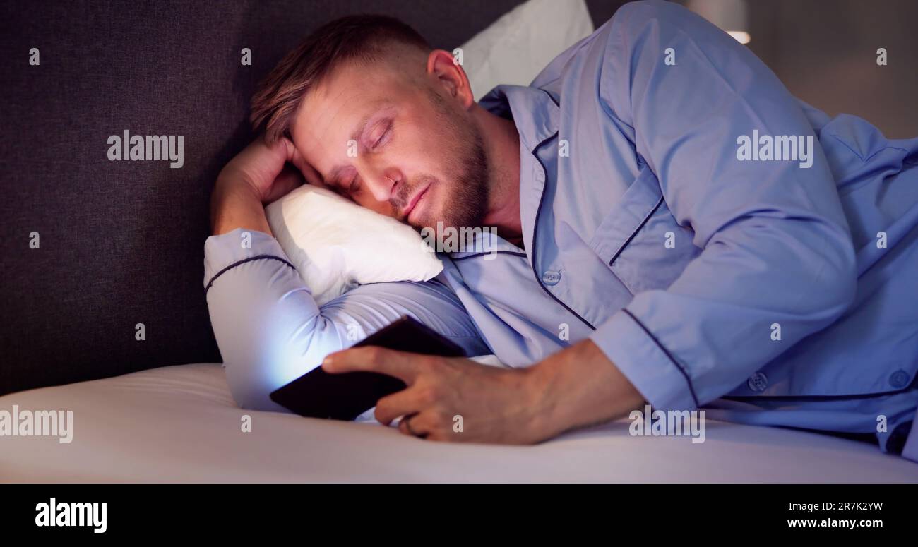 L'homme au lit avec un téléphone mobile dans la nuit Banque D'Images