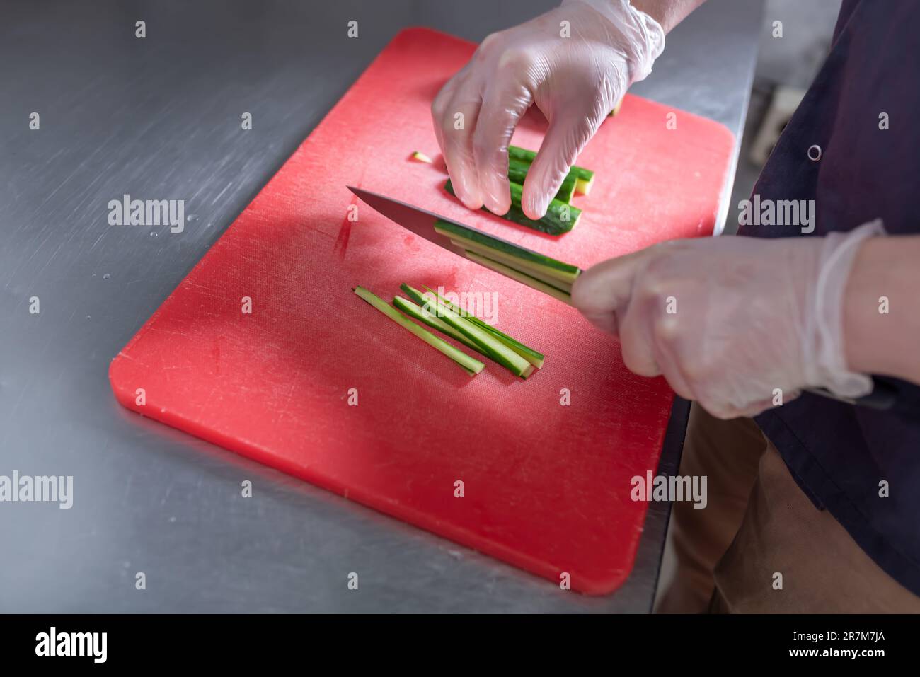 Le cuisinier coupe le concombre pour les petits pains à sushis sur un tableau rouge. Photo de haute qualité Banque D'Images