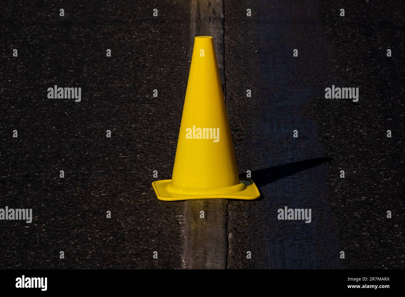 le cône de signalisation jaune se trouve sur la ligne de signalisation routière sur l'asphalte foncé Banque D'Images