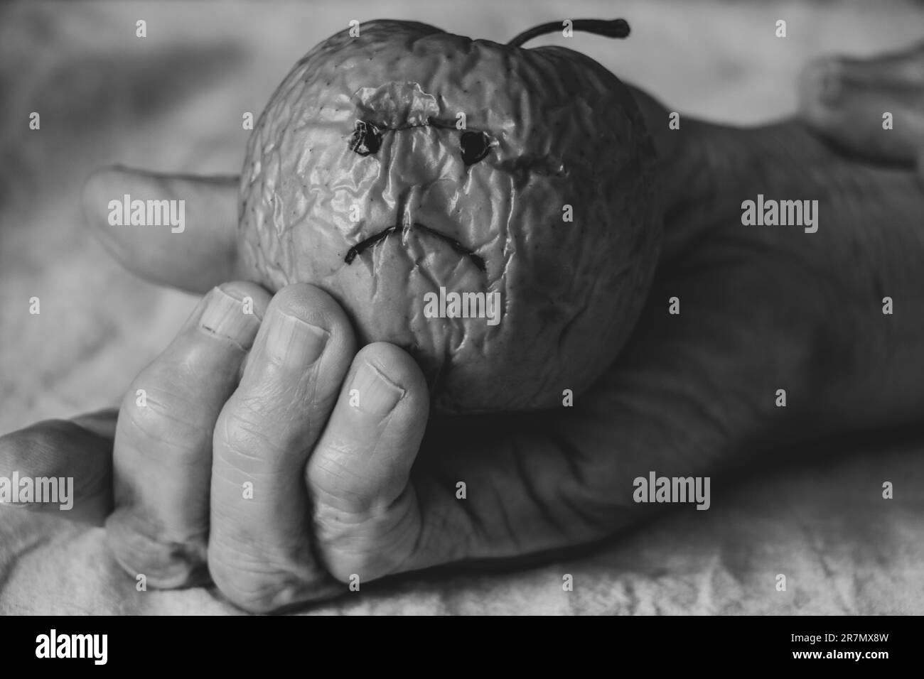 Une pomme sèche lente avec un triste sourire dans les mains d'une vieille femme, la faim et une mauvaise récolte, la tristesse et la colère Banque D'Images