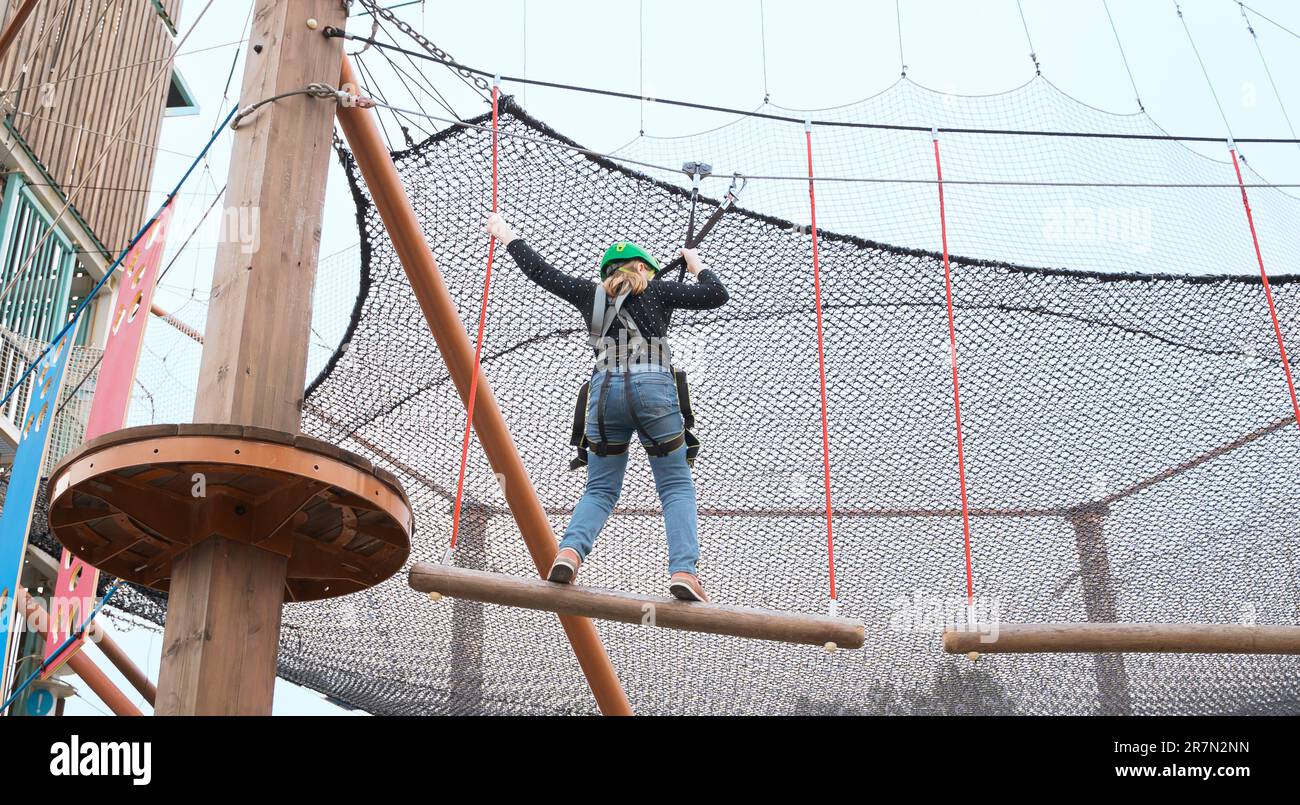 Adolescente dans l'équipement de harnais d'escalade, casque de sécurité vert de sport. Parc d'attractions de corde. Fixation fixant le mousqueton à la corde de sécurité. Hangin Banque D'Images