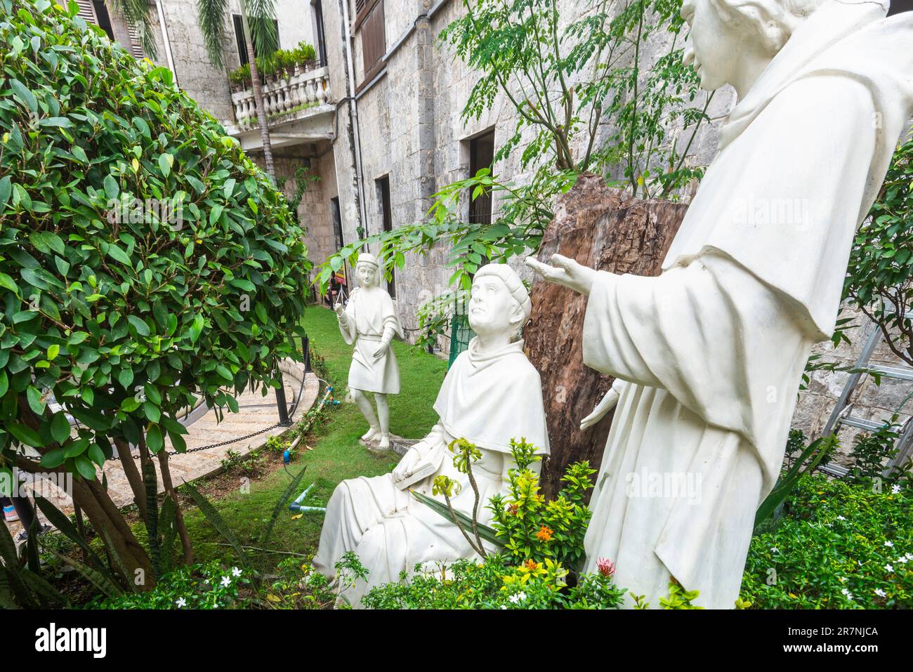 Statues blanches de saints, icônes catholiques historiques, et la figure d'un enfant, positionné comme si dans une conversation décontractée, parmi le feuillage bien gardé, les plantes et Banque D'Images