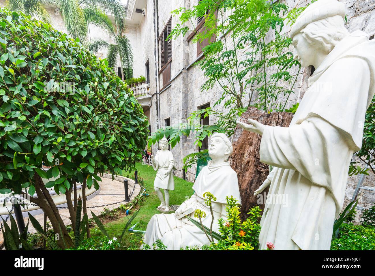 Cebu,Philippines-17 janvier 2023: Statues d'icônes catholiques historiques, et la figure d'un enfant, positionné comme si dans la conversation, parmi les plantes luxuriantes an Banque D'Images
