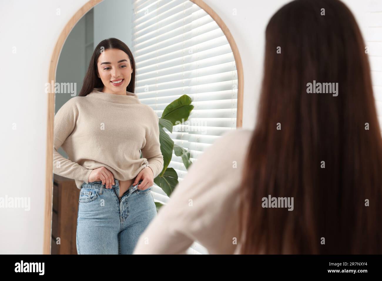 Jeune femme en Jean élégant près du miroir à l'intérieur Banque D'Images